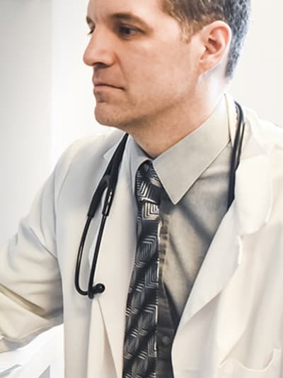 Medical professional wearing white coat and stethoscope reviews medical images on a desktop computer.